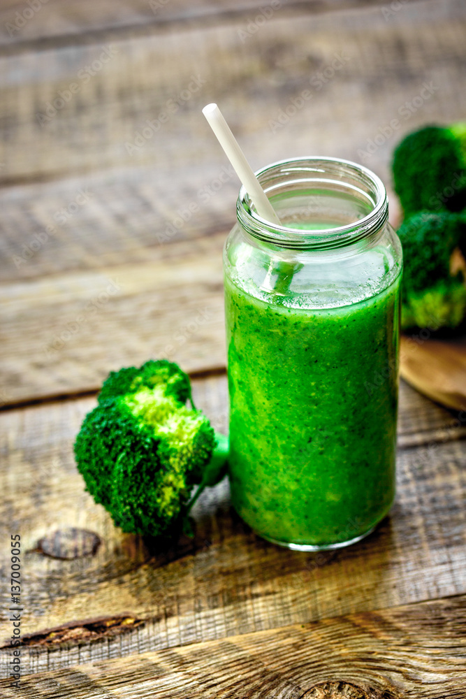 Green vegetable smoothie in glass at wooden background