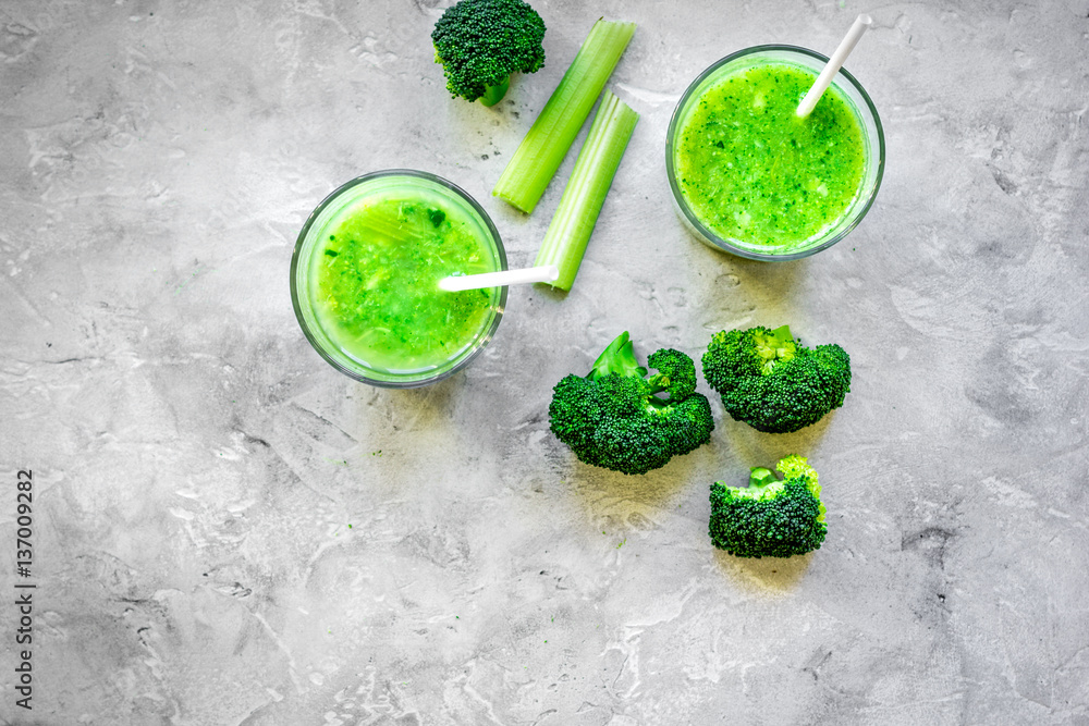 Green vegetable smoothie in glass at gray background top view