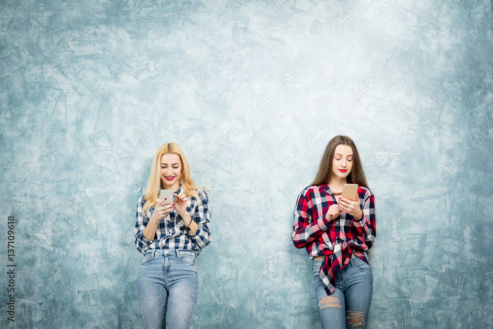 Female friends using smart phones on the blue wall background. Wide shot with copy space