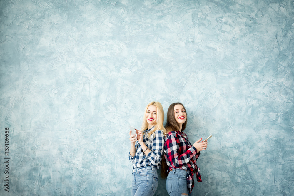 Female friends using smart phones on the blue wall background. Wide shot with copy space