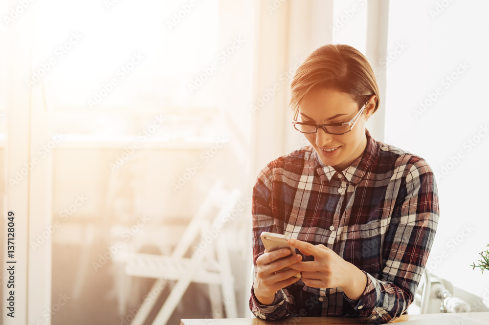 Portrait of a charming young woman reading a text message on mobile phone, lens flare