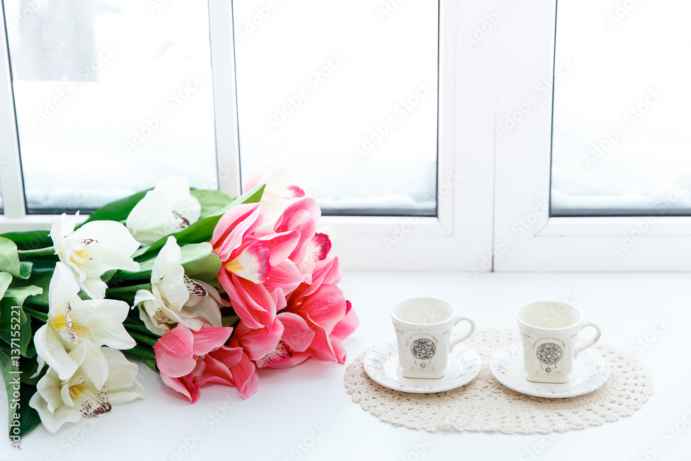 beautiful red tulips in vase and two cups on a window sill.