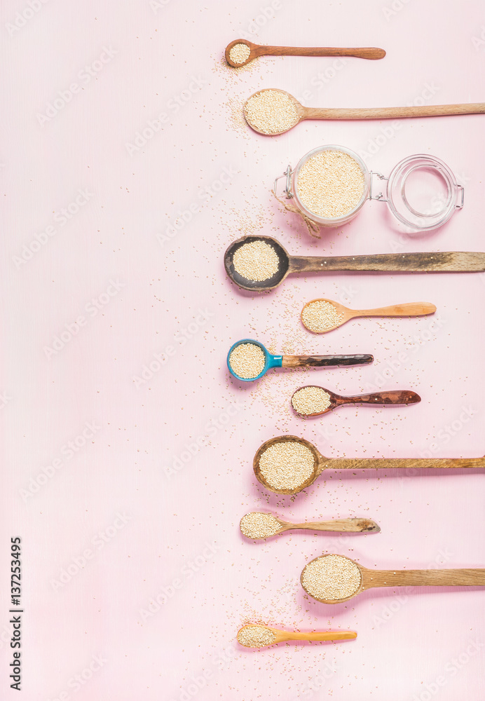 Quinoa seeds in different spoons and glass jar over light pink background, top view, copy space. Sup