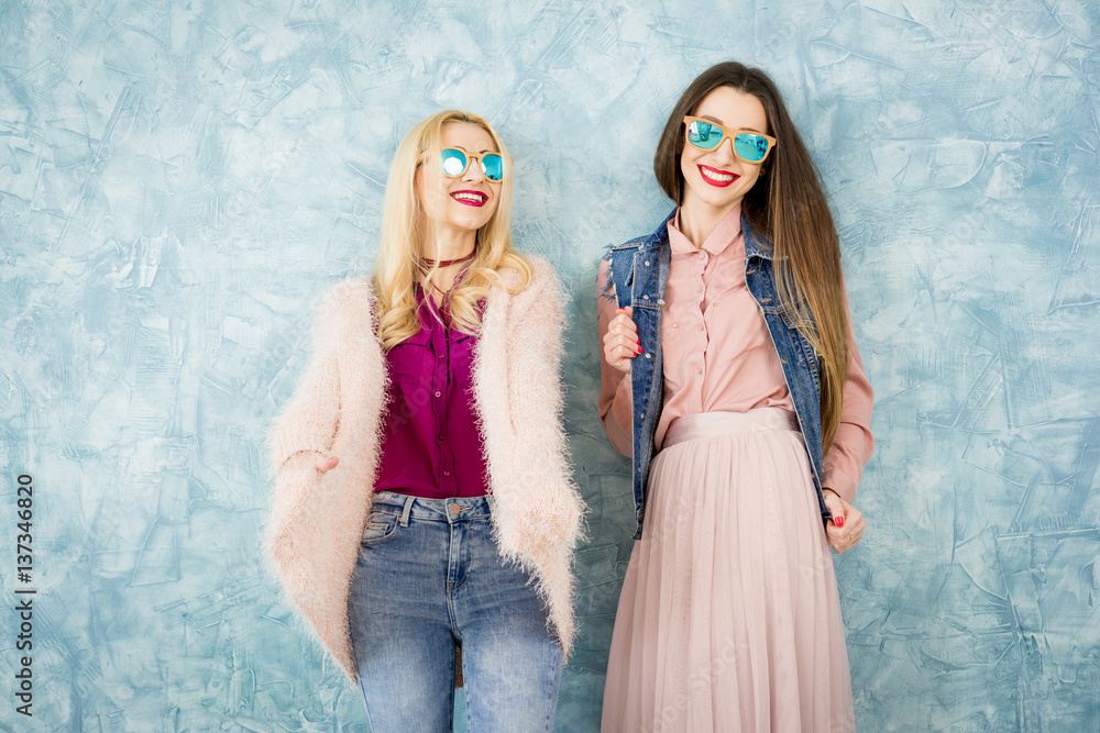 Female stylish friends having fun together on the blue wall background