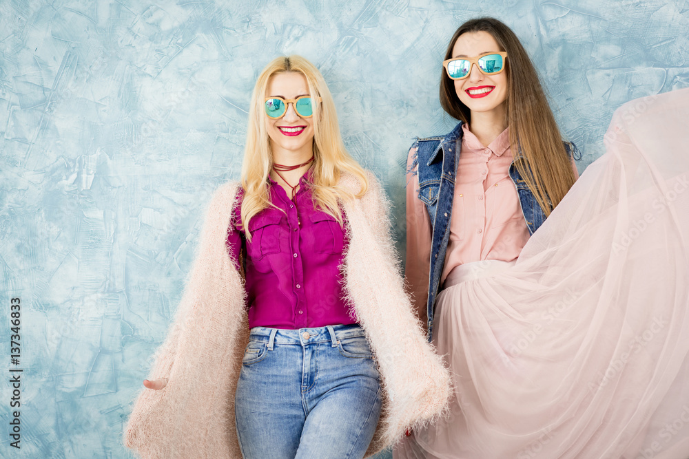 Female stylish friends having fun together on the blue wall background