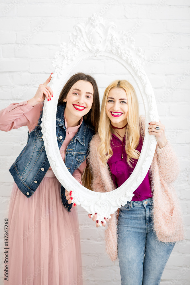 Portrait of two women friends in the frame on the white wall background