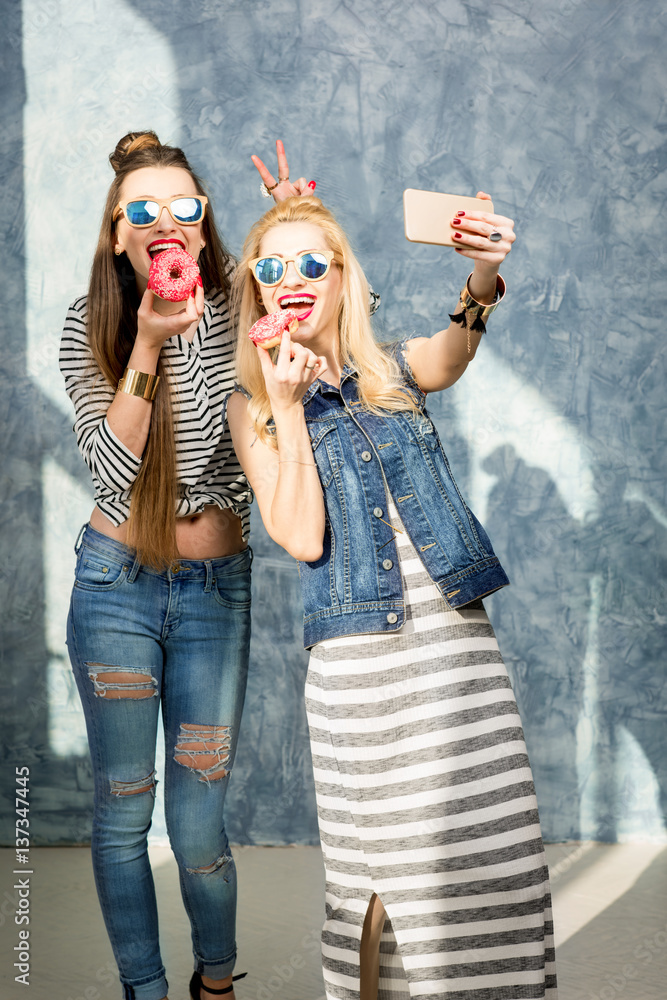 Playful women having fun with sweet donuts on the blue wall background