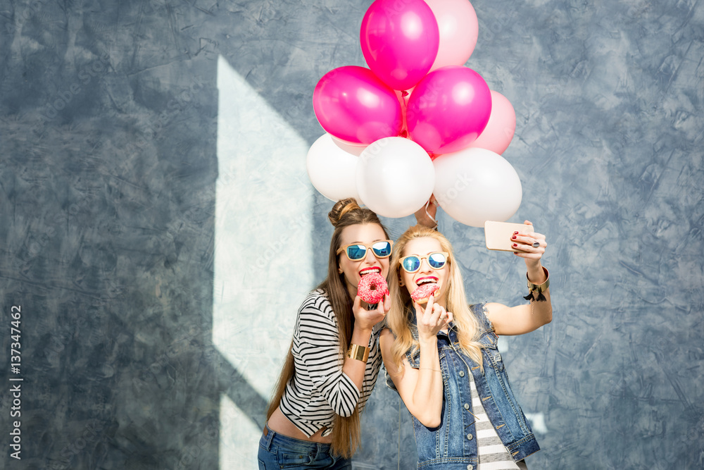 Playful women having fun with sweet donuts and baloons on the blue wall background