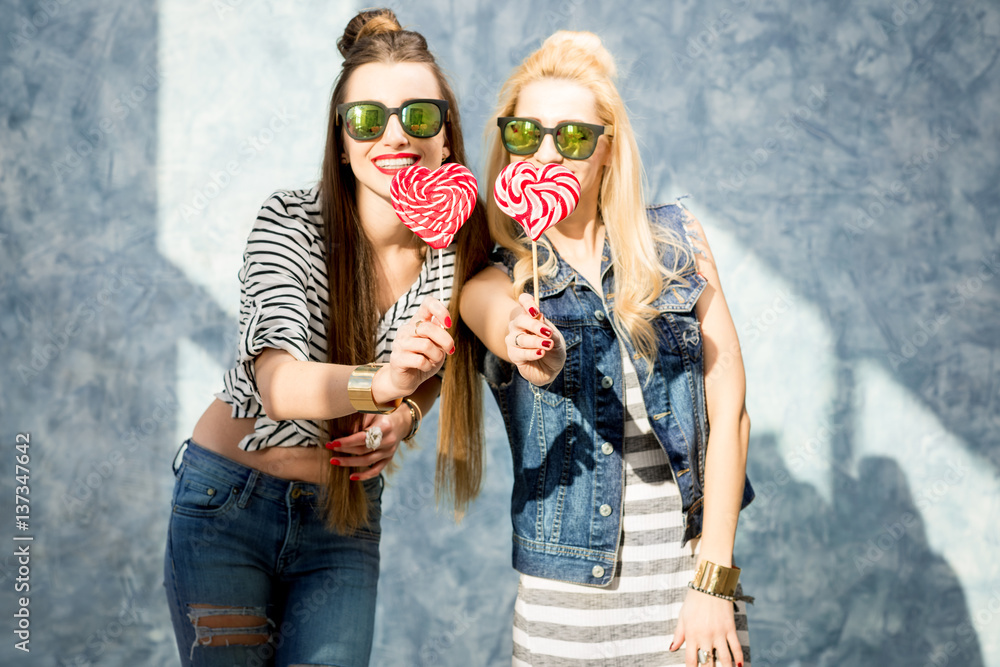 Young female friends having fun with candies standing on the blue wall background