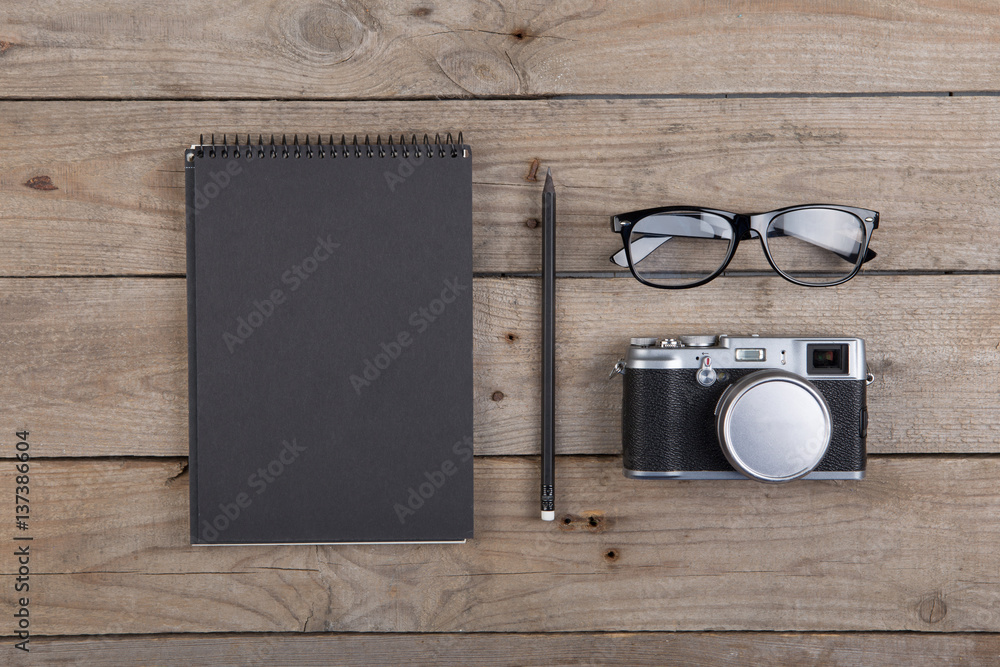 Notepad, glasses and camera on the wooden desk