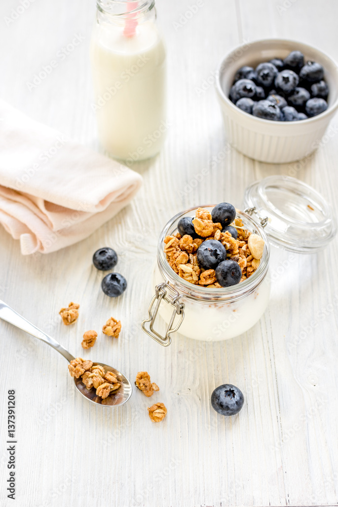 Homemade granola with blueberries in jar on white kitchen background