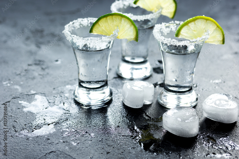 Tequila shot with lime slices and salt on dark background