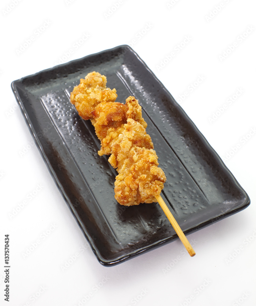 Crispy deep fried chicken with skewer and black plate on white background