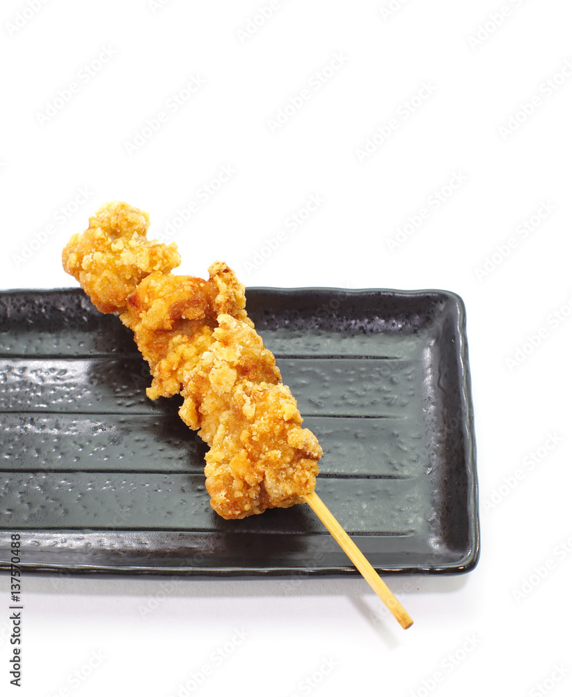 Crispy deep fried chicken with skewer and black plate on white background