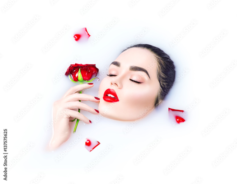 Beautiful model girl with bright makeup holding red rose flower in her hand and relaxing in milk bat