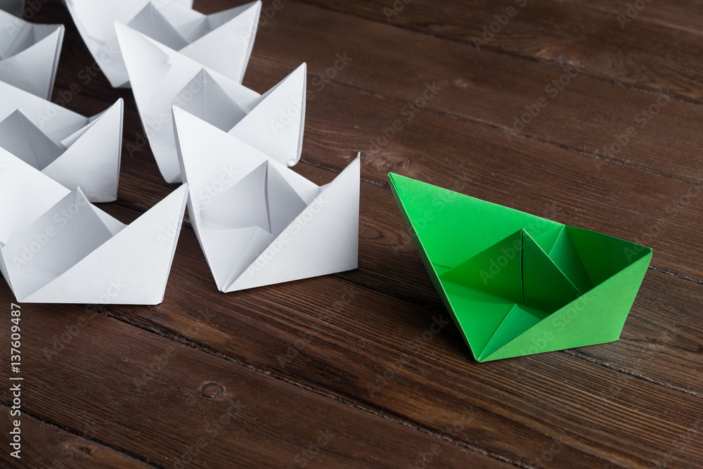 Business leadership concept with white and color paper boats on wooden table