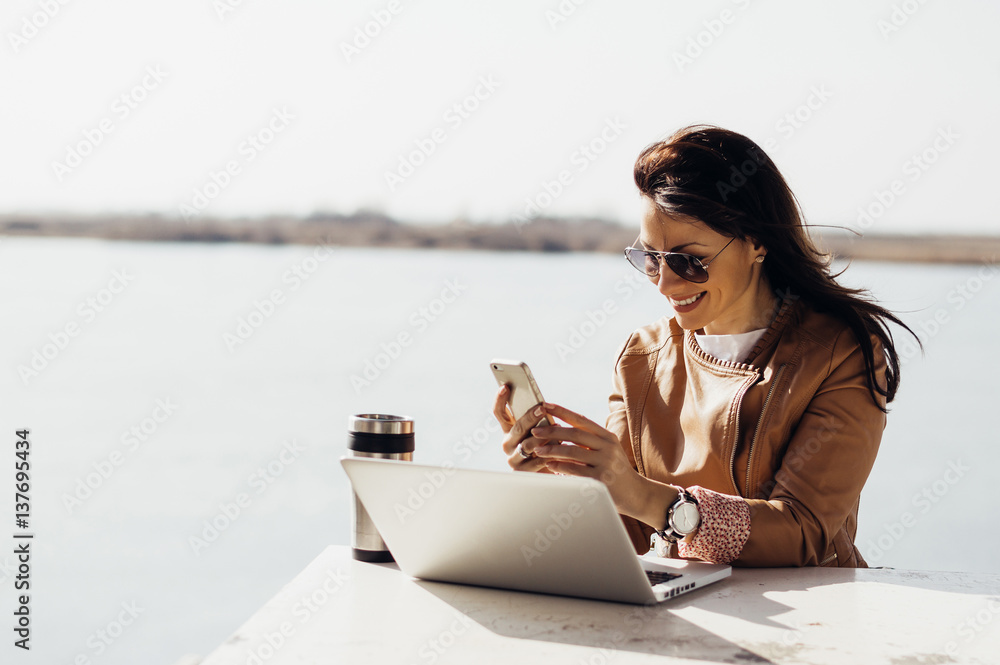 Portrait of young attractive businesswoman checking emails on the phone outdoors