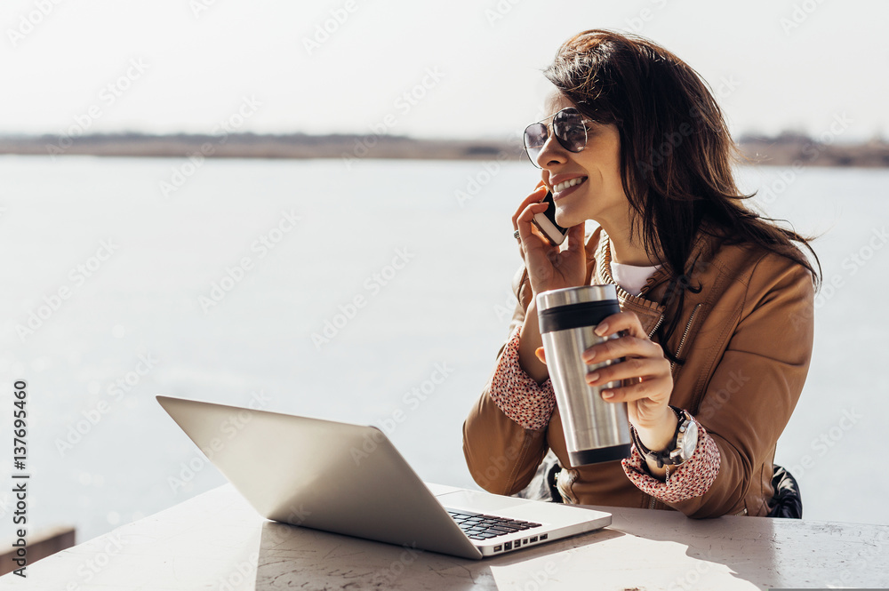 Portrait of young attractive businesswoman talking on the phone while holding coffee outdoors