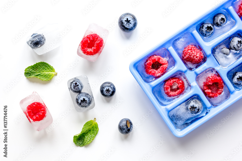 Ice tray with berries and mint on white background top view