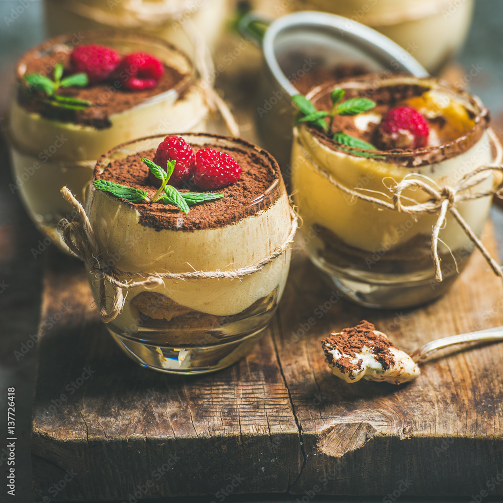 Homemade Italian dessert Tiramisu served in individual glasses with mint leaves, fresh raspberries a