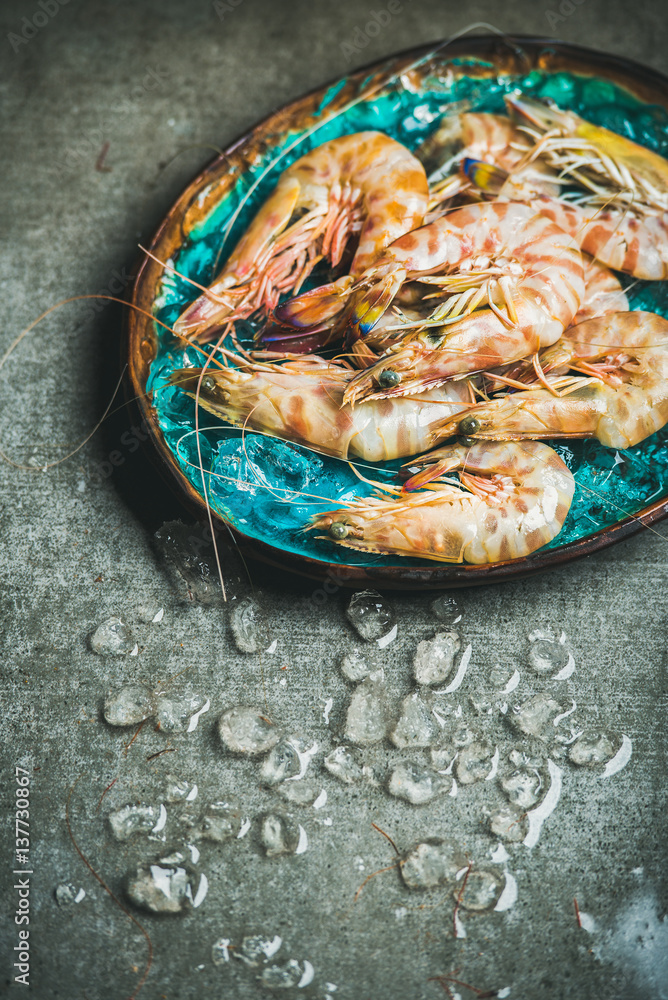 Raw uncooked tiger prawns on chipped ice in turquoise blue ceramic tray over grey concrete backgroun