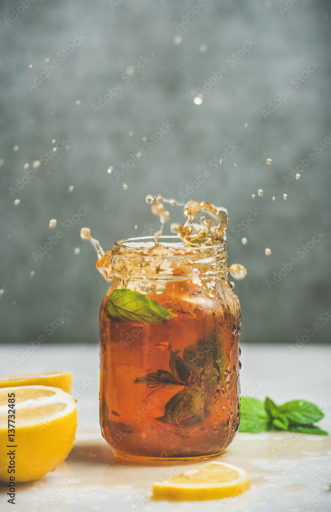 Summer cold Iced tea with fresh bergamot, mint and lemon in glass jar with splashes, grey concrete w