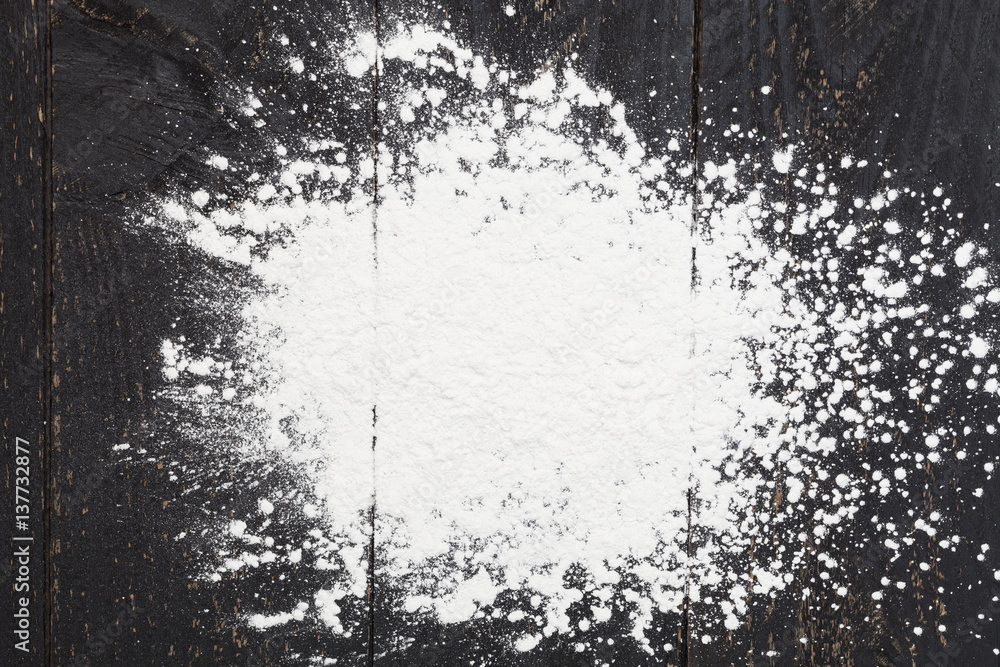 sprinkle wheat flour with copy space for text on dark black wood background, top view for cooking do