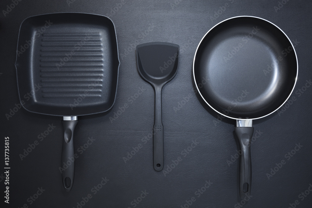 Top view frying pan and plastic spade on black table background.