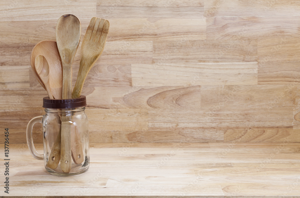 Wooden spoon and fork in glass bottle on wood background.