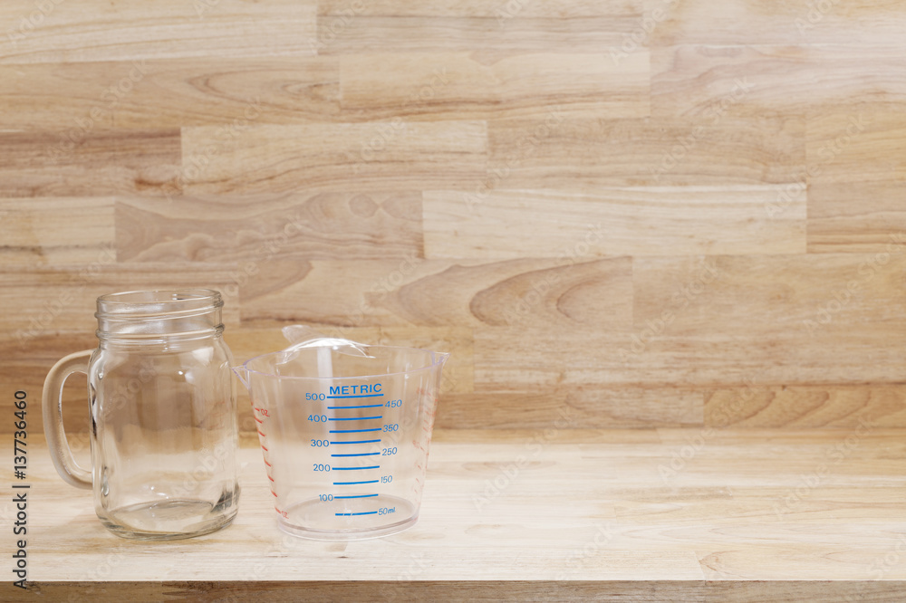 glass bottle and empty measuring cup on wooden background.