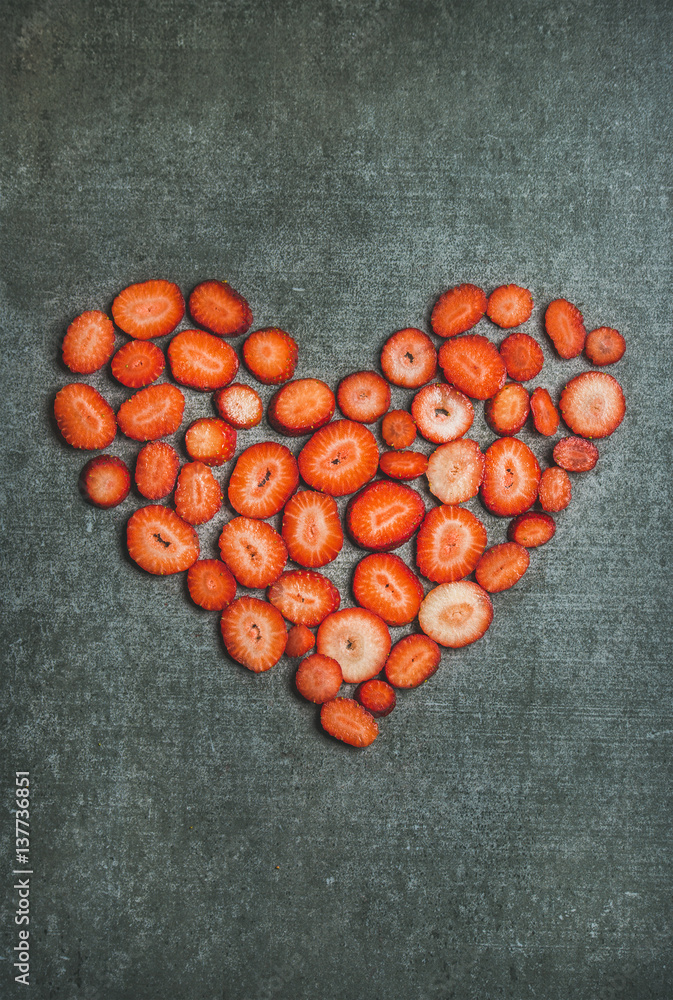 Pieces of fresh red strawberry placed in shape of heart over grey concrete background, top view, cop