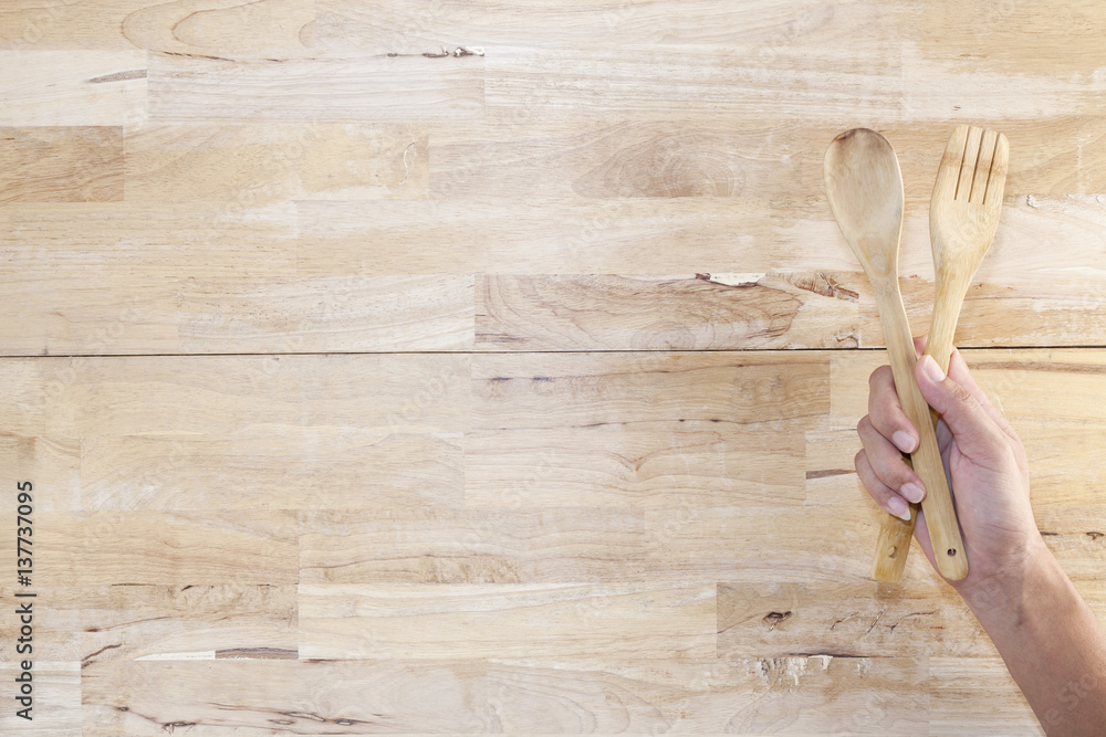 Hand holding a wooden spoon on wood background.