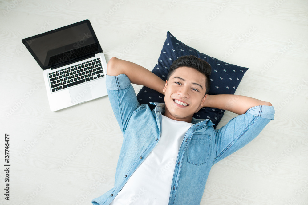 Top view of asian man lying on the floor with laptop, camera, tablet, coffee and phone