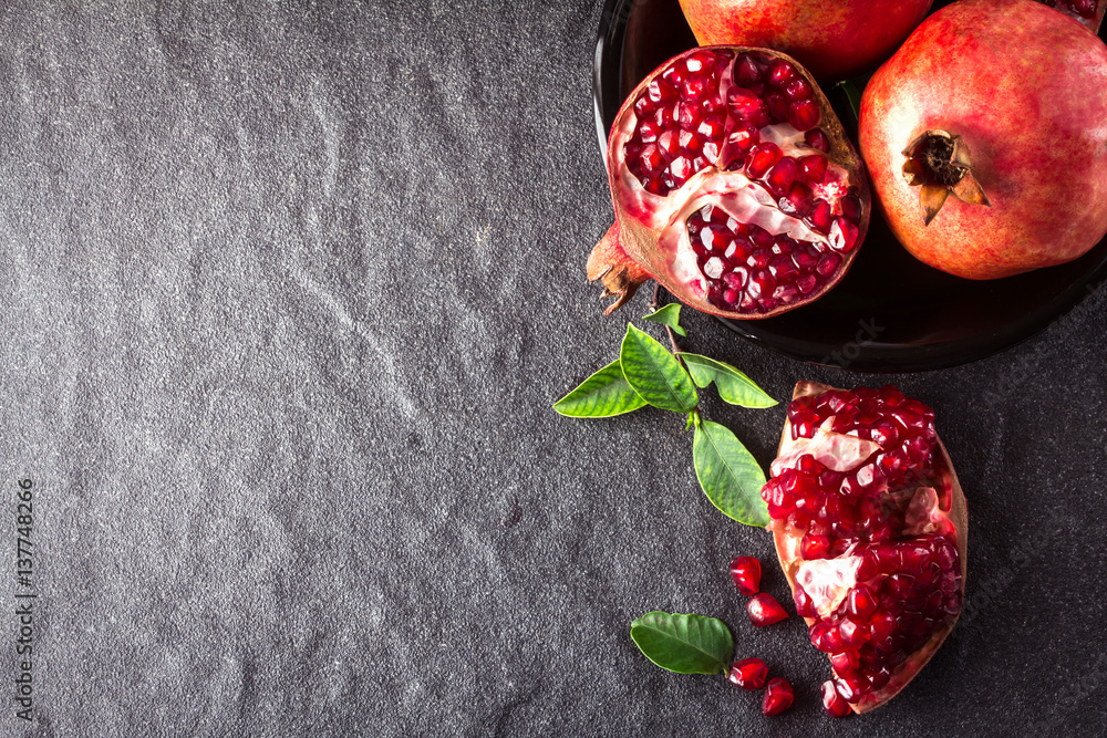 Fresh red pomegranate and seed  with leaves over black stone background , overhead or top view