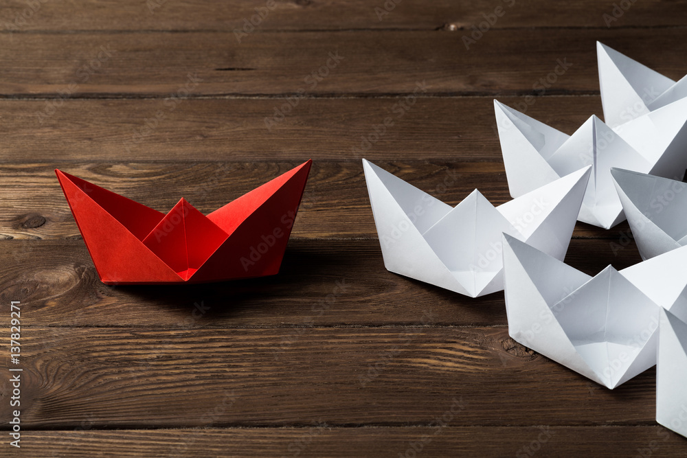 Business leadership concept with white and color paper boats on wooden table