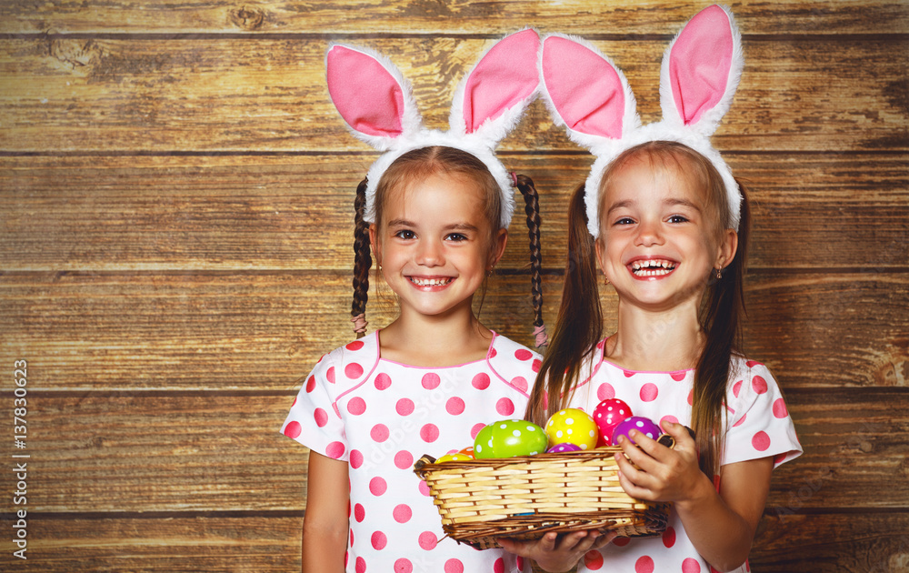 Happy easter! cute twins girls sisters dressed as rabbits with eggs on wooden background