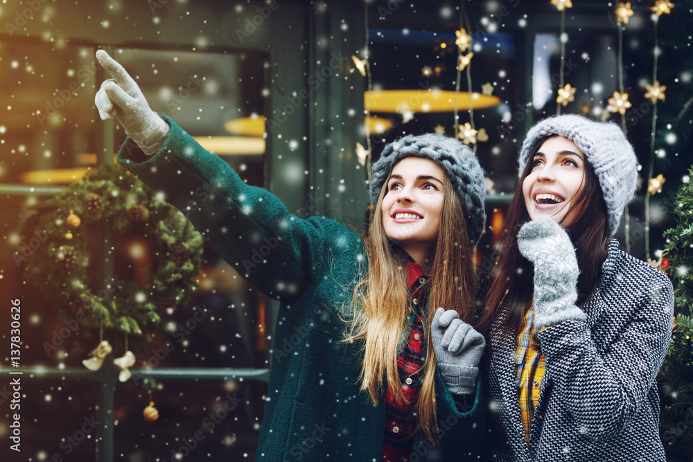 Outdoor waist up portrait of two young beautiful fashionable happy smiling surprised girls posing on