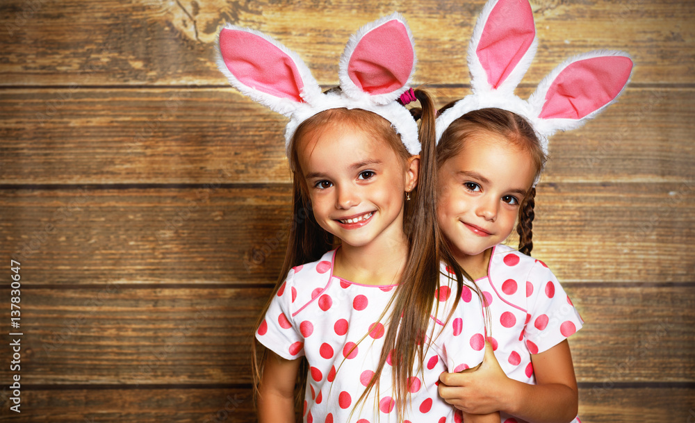 Happy easter! cute twins girls sisters dressed as rabbits  on wooden background