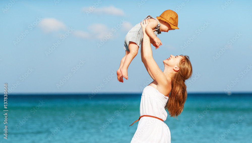 happy family mother with baby son walks by ocean on beach in summer