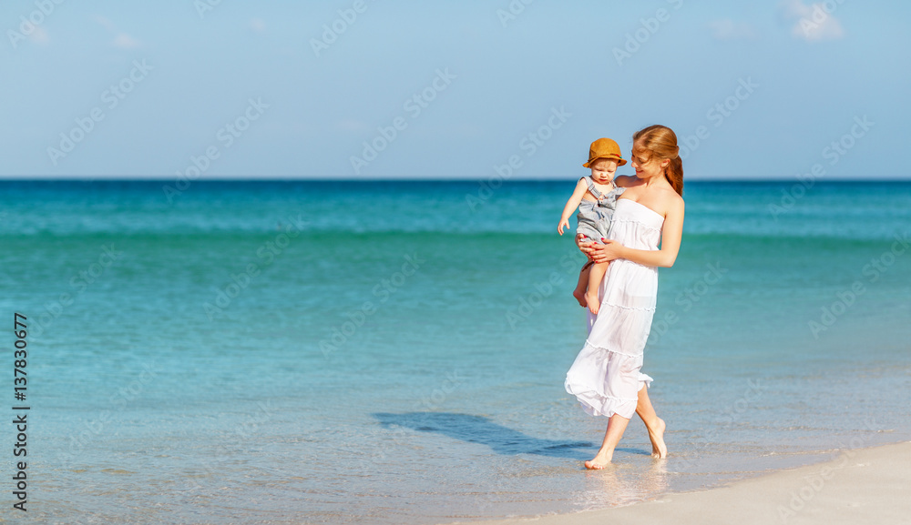 happy family mother with baby son walks by ocean on beach in summer