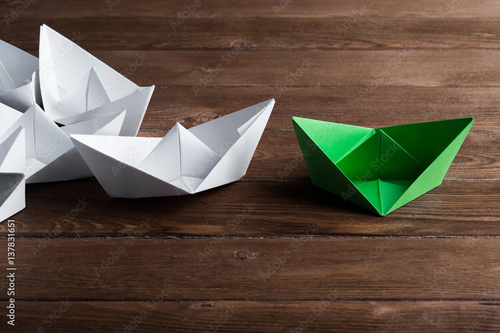 Business leadership concept with white and color paper boats on wooden table