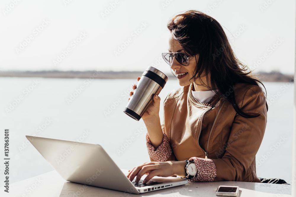 Adult woman working remotely. Freelancing outdoors. Woman drinking coffee and working on laptop comp