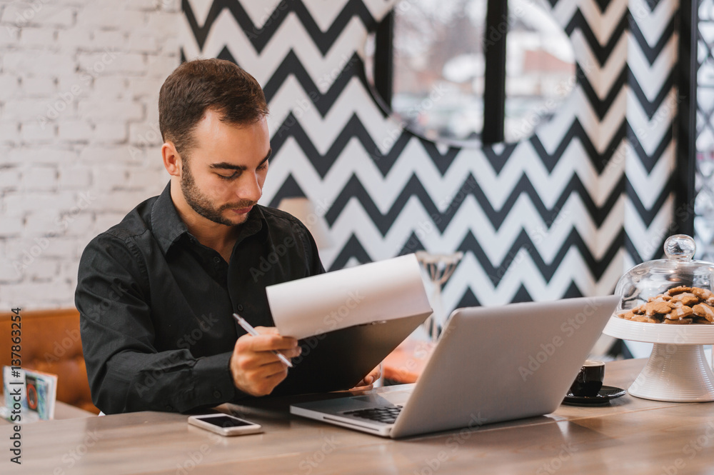 Handsome guy with laptop checking menu at city restaurant