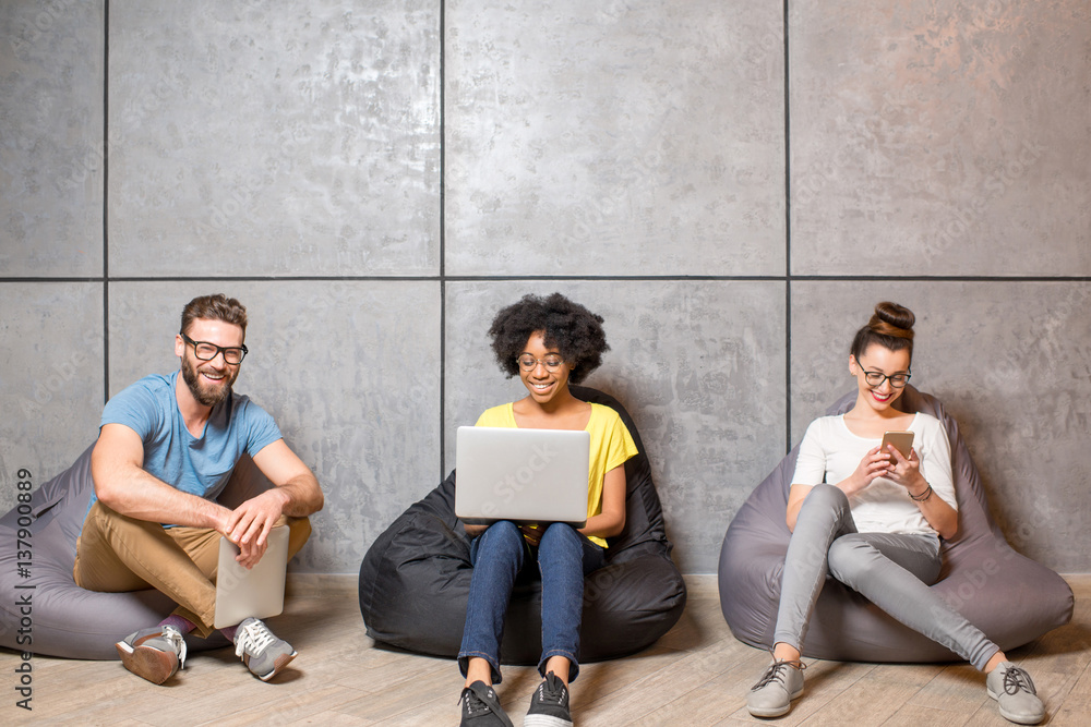 Multi ethnic coworkers dressed casually in colorful clothes working with different gadgets sitting o