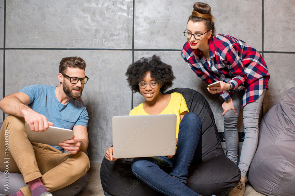 Multi ethnic coworkers dressed casually in colorful clothes working together with different gadgets 