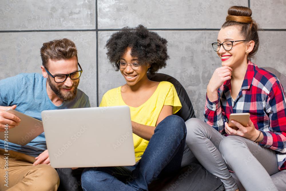 Multi ethnic coworkers dressed casually in colorful clothes working together with different gadgets 