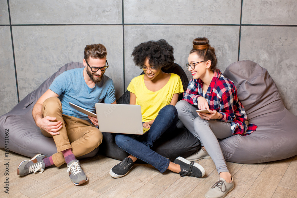 Multi ethnic coworkers dressed casually in colorful clothes working together with different gadgets 