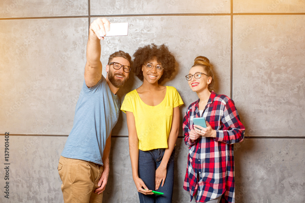 Multi ethnic coworkers dressed casually in colorful clothes making selfie photo with smart phone sta