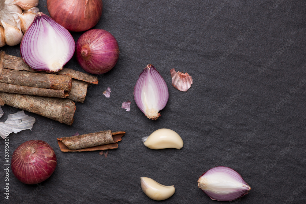 Cooking ingredients: cinnamon sticks and garlic on black stone table.