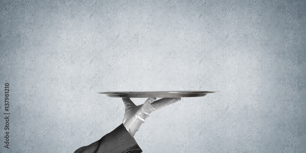 Hand of butler holding empty metal tray against concrete background